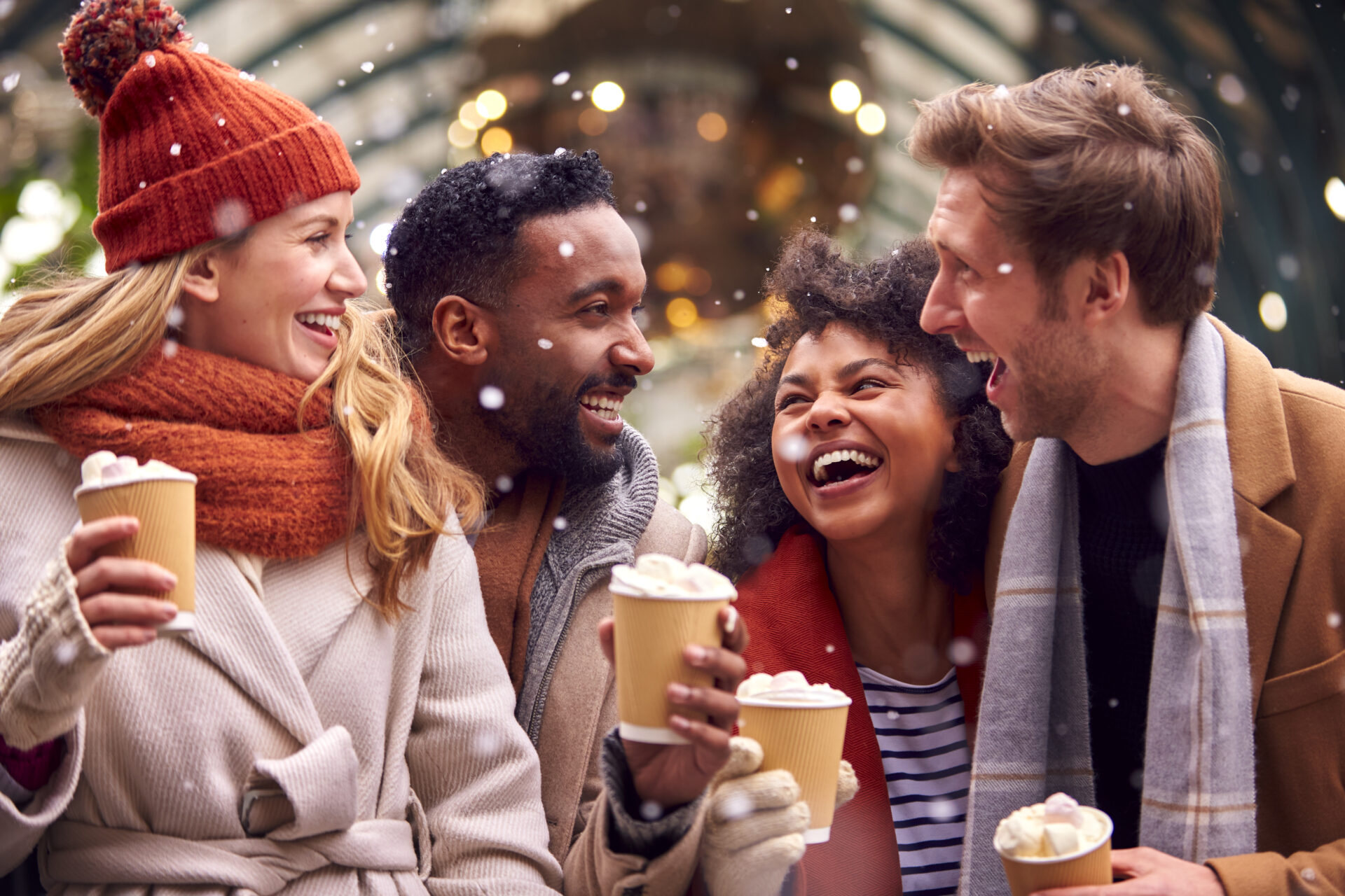 Group Of Friends Drinking Hot Chocolate With Marshmallows In Snow At Outdoor Christmas Market