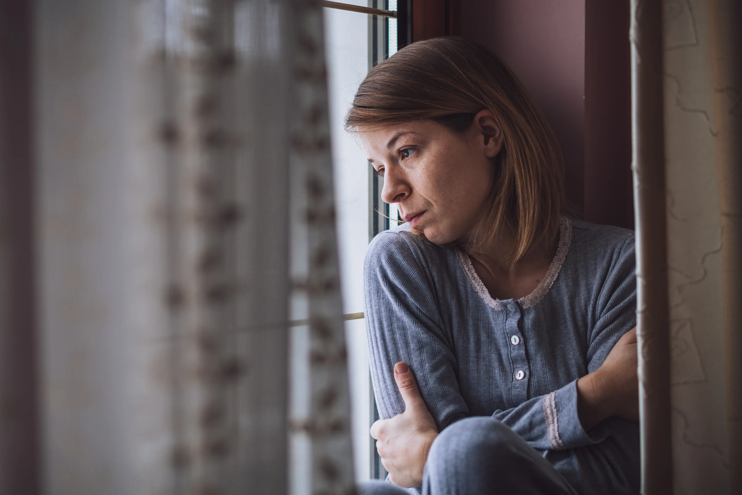 Sad woman sitting by the window looking outside