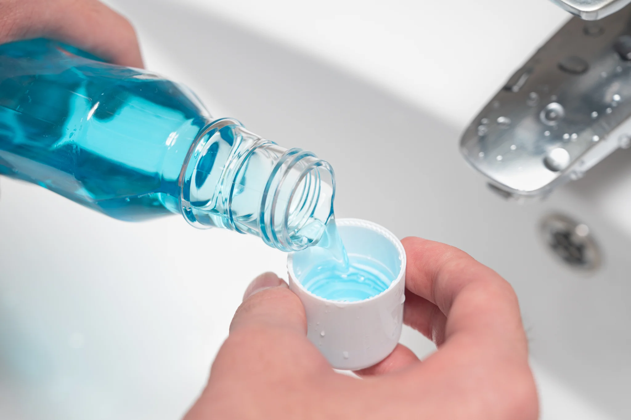 Mouthwash being poured into a cup over a bathroom sink