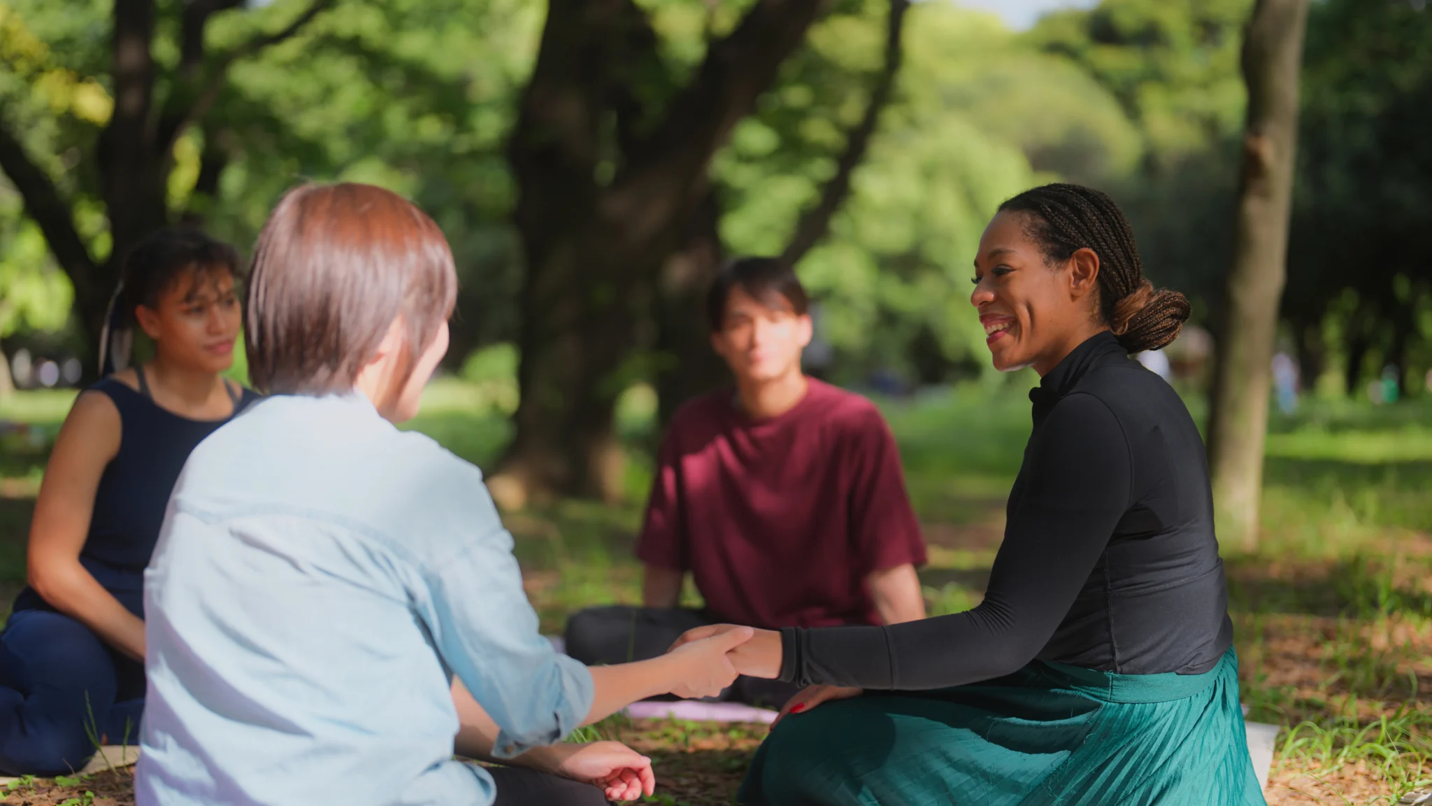 A multi-ethnic group of people are meeting in nature for a group therapy session. They talk listen and console each other.