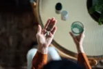 Overhead view of woman holding pills in left hand and glass of water in right hand