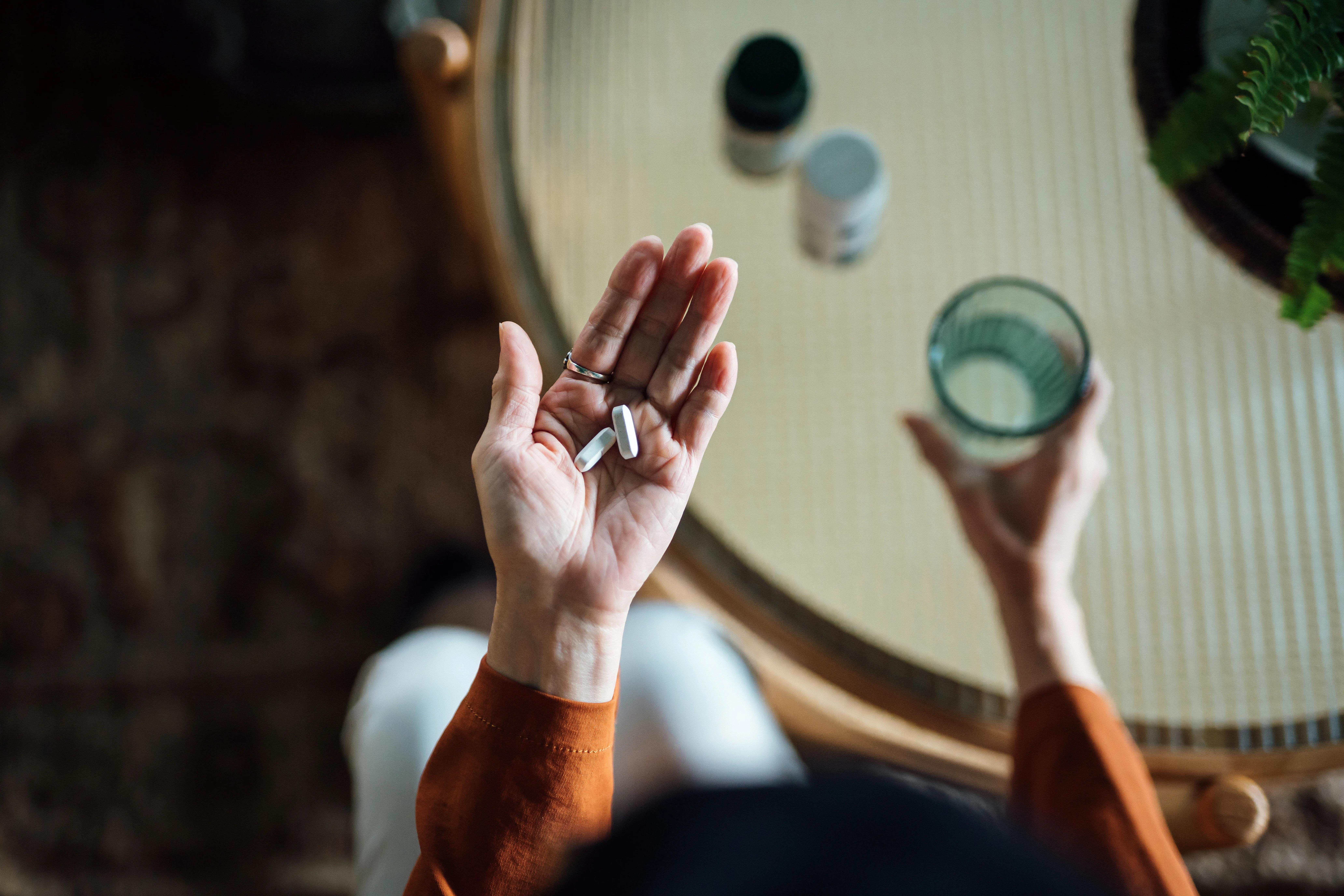 Overhead view of woman holding pills in left hand and glass of water in right hand