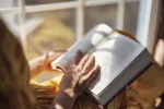 Woman enjoying reading a book by a sunny window