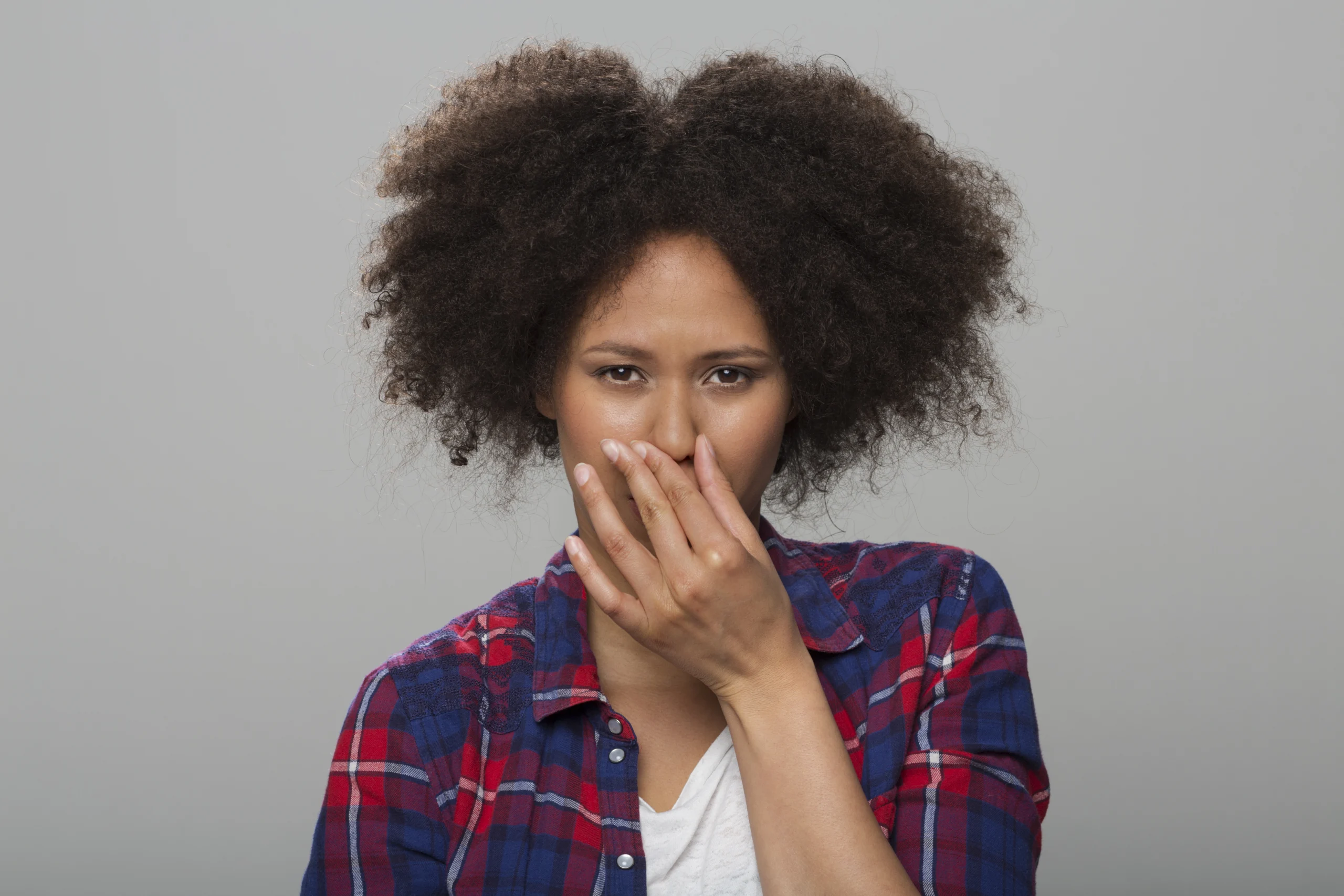 Portrait of young woman holding nose while standing against grey background.
