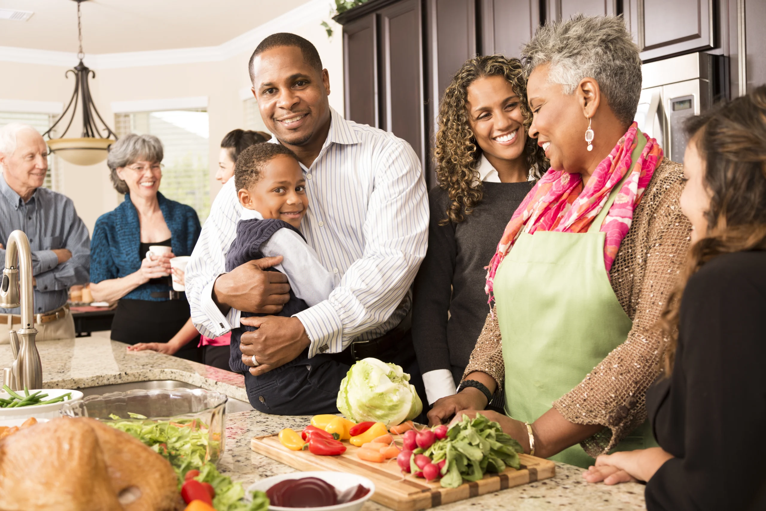 Family, friends and neighbors gather together in senior woman's home to prepare Thanksgiving dinner. They all work together in the kitchen. Roasted turkey and salad ingredients on counter. Multi-ethnic and mixed age group of people. Latin, African, and Caucasian ethnicities.