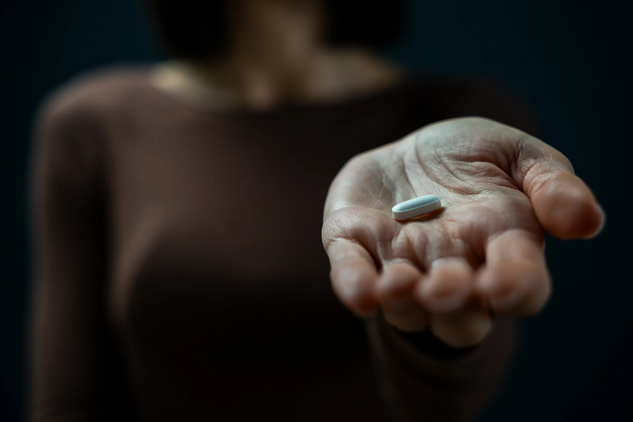 A woman holds a white tablet in dark setting, symbolizing drug addiction and the emotional tension behind substance use.