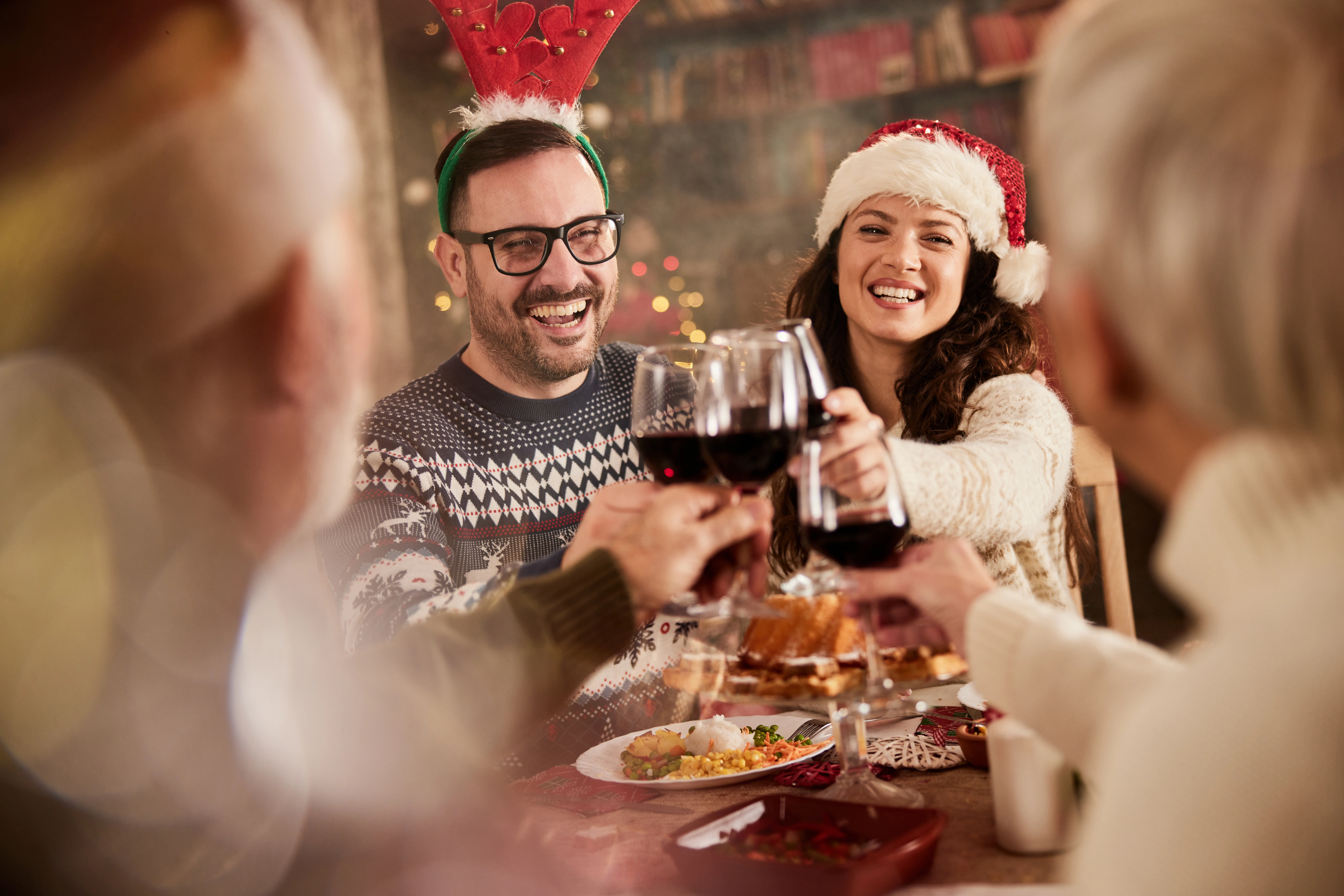 Young happy couple toasting with senior couple while having New Year's lunch in dining room.