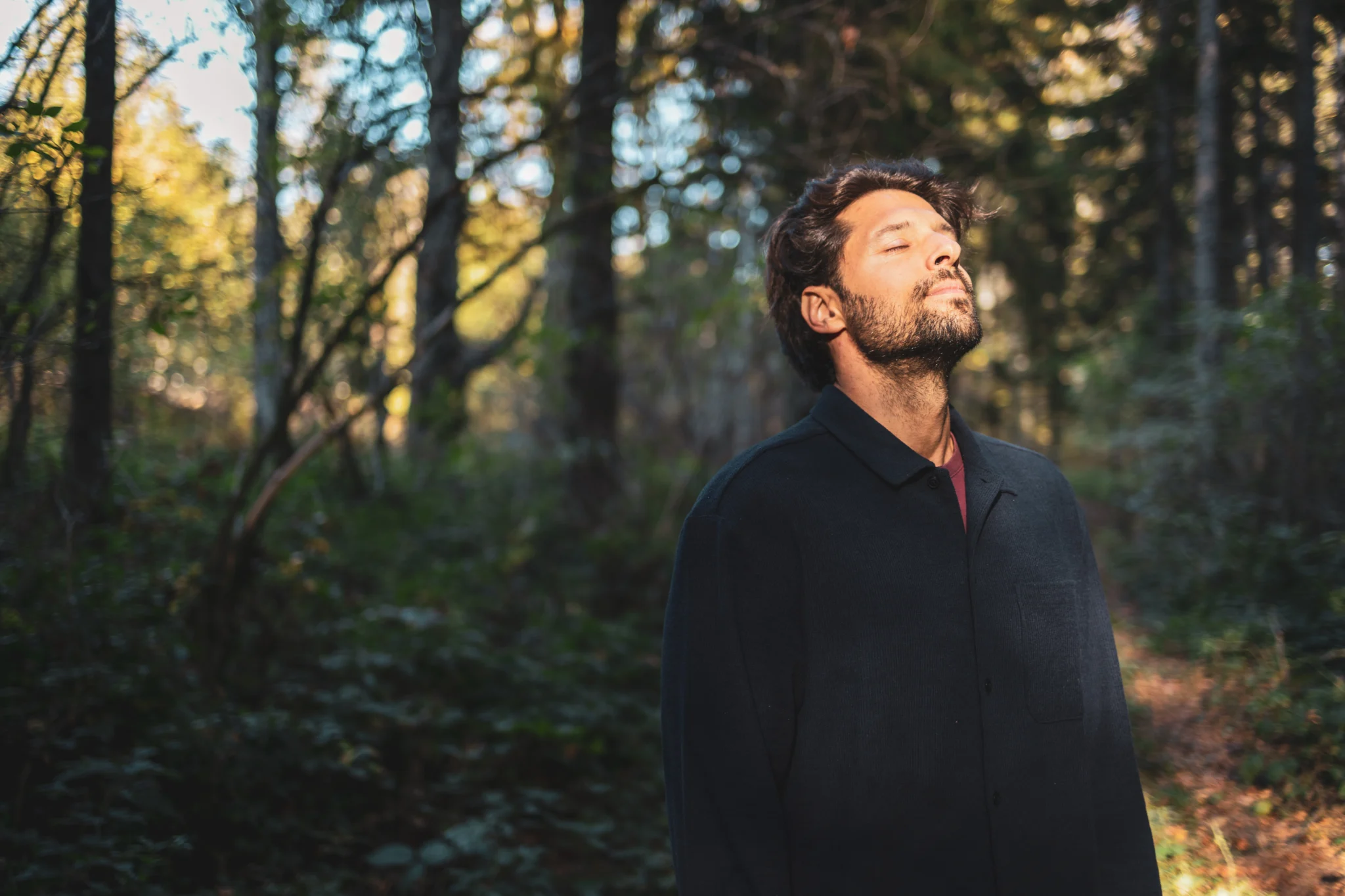 Man standing in the forest with his eyes closed enjoying the sun